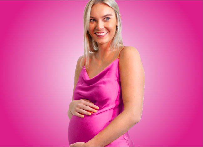 Pregnant, blonde woman in a pink dress, holds her belly