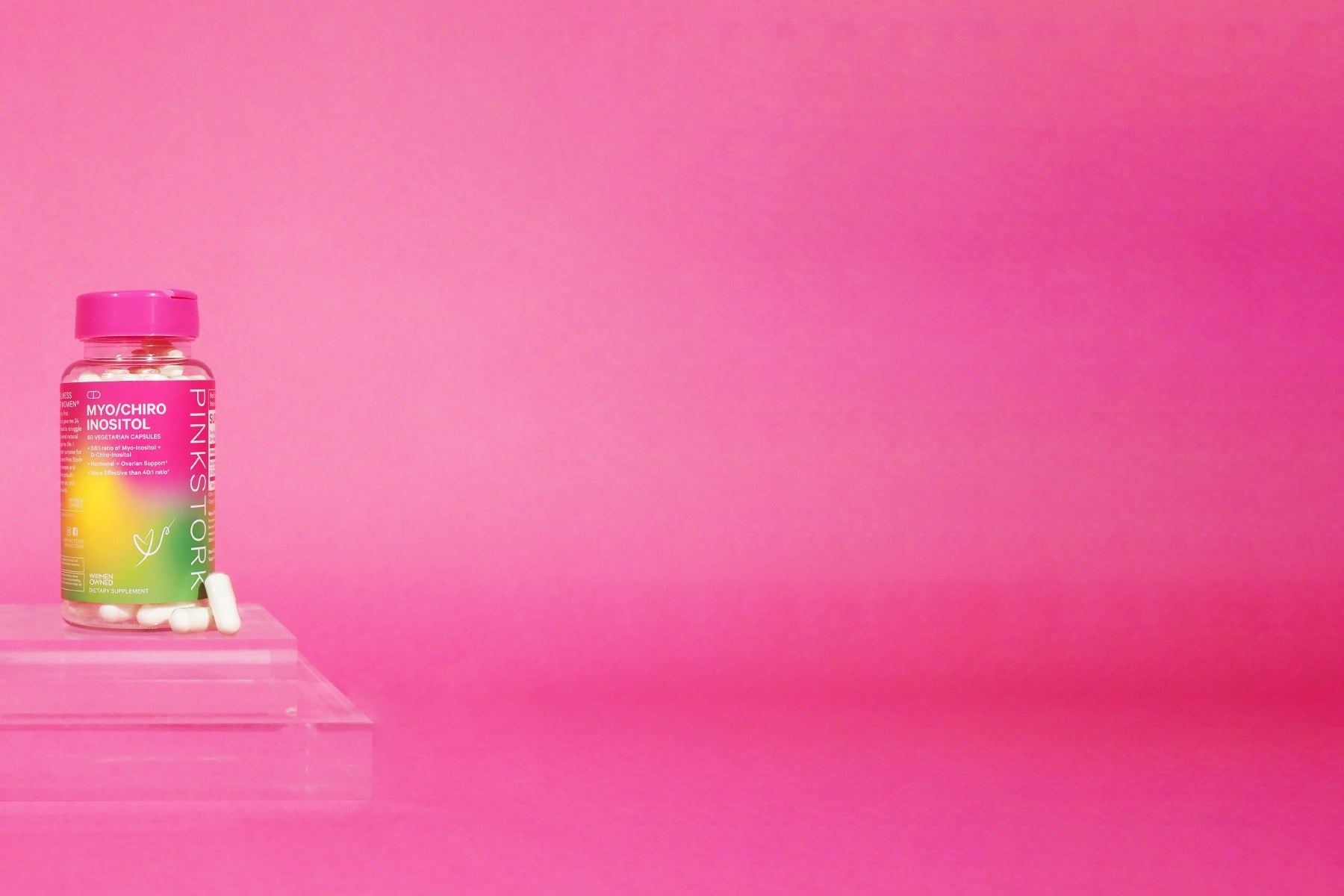 Pink Stork Myo/Chiro Inositol supplement bottle with capsules on a clear stand against a bright pink gradient background.