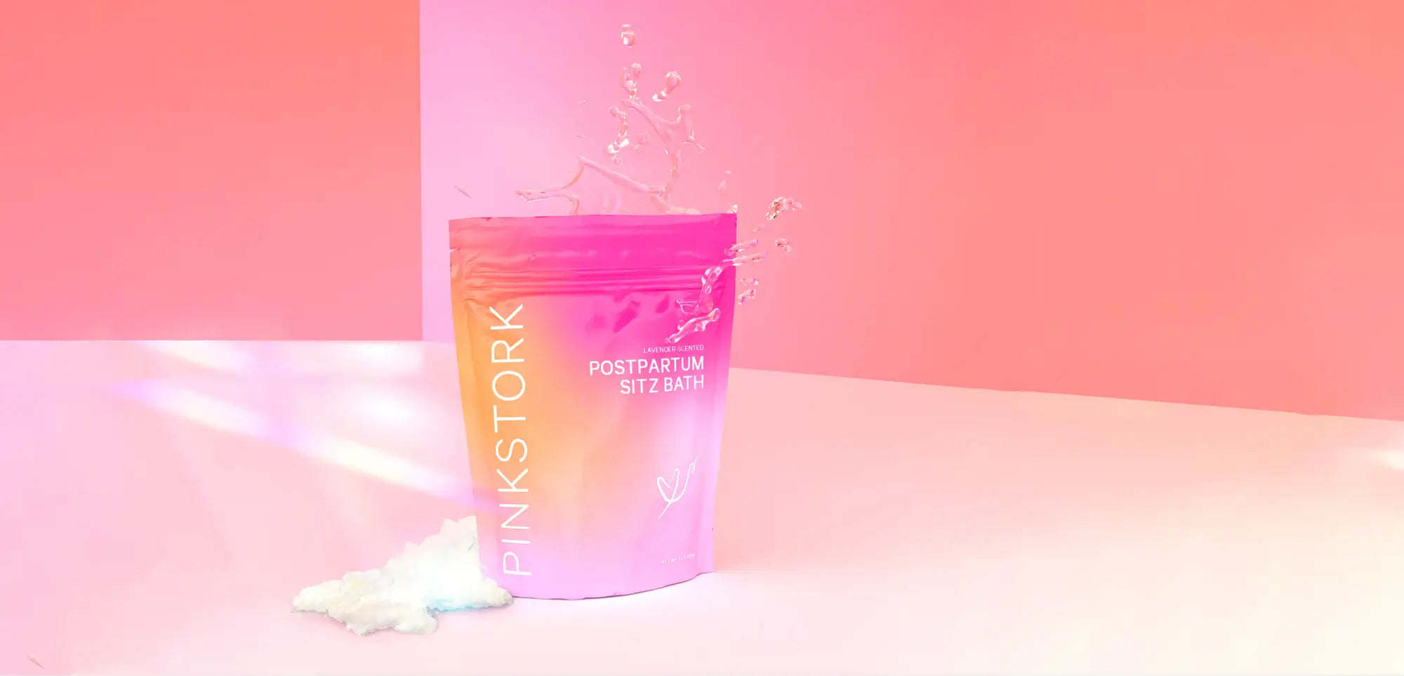 Pink Stork Postpartum Sitz Bath product with splash effect on pink background.