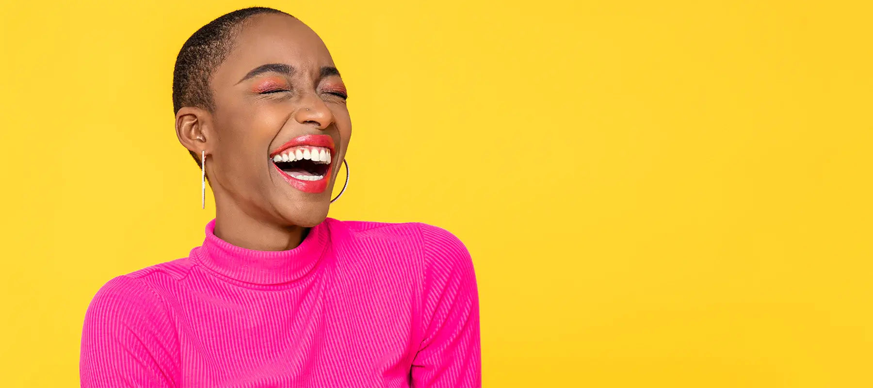 Joyful woman in a bright pink turtleneck laughing against a vibrant yellow background.
