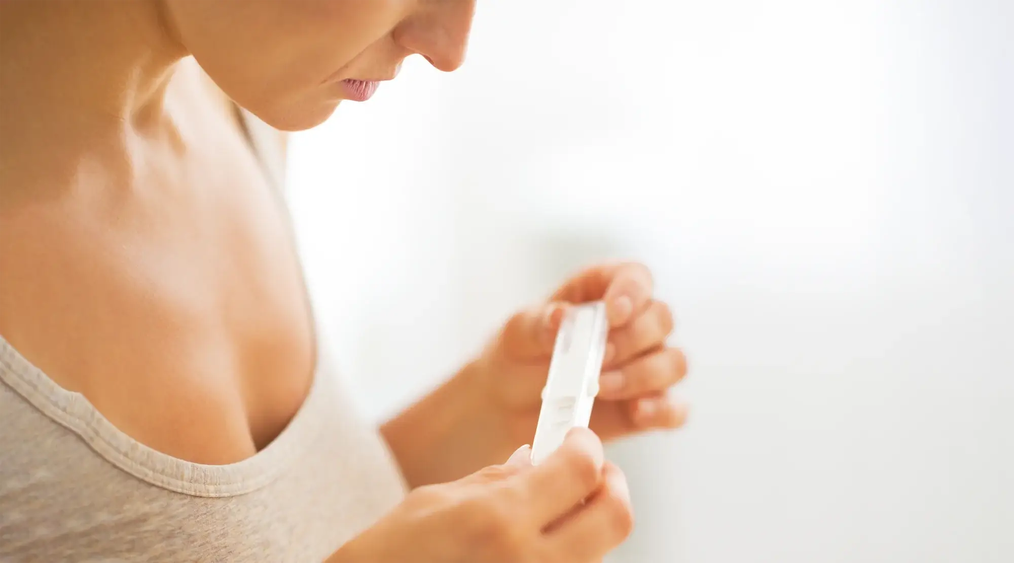 Close-up of a woman closely examining a pregnancy test at home, highlighting fertility and conception.