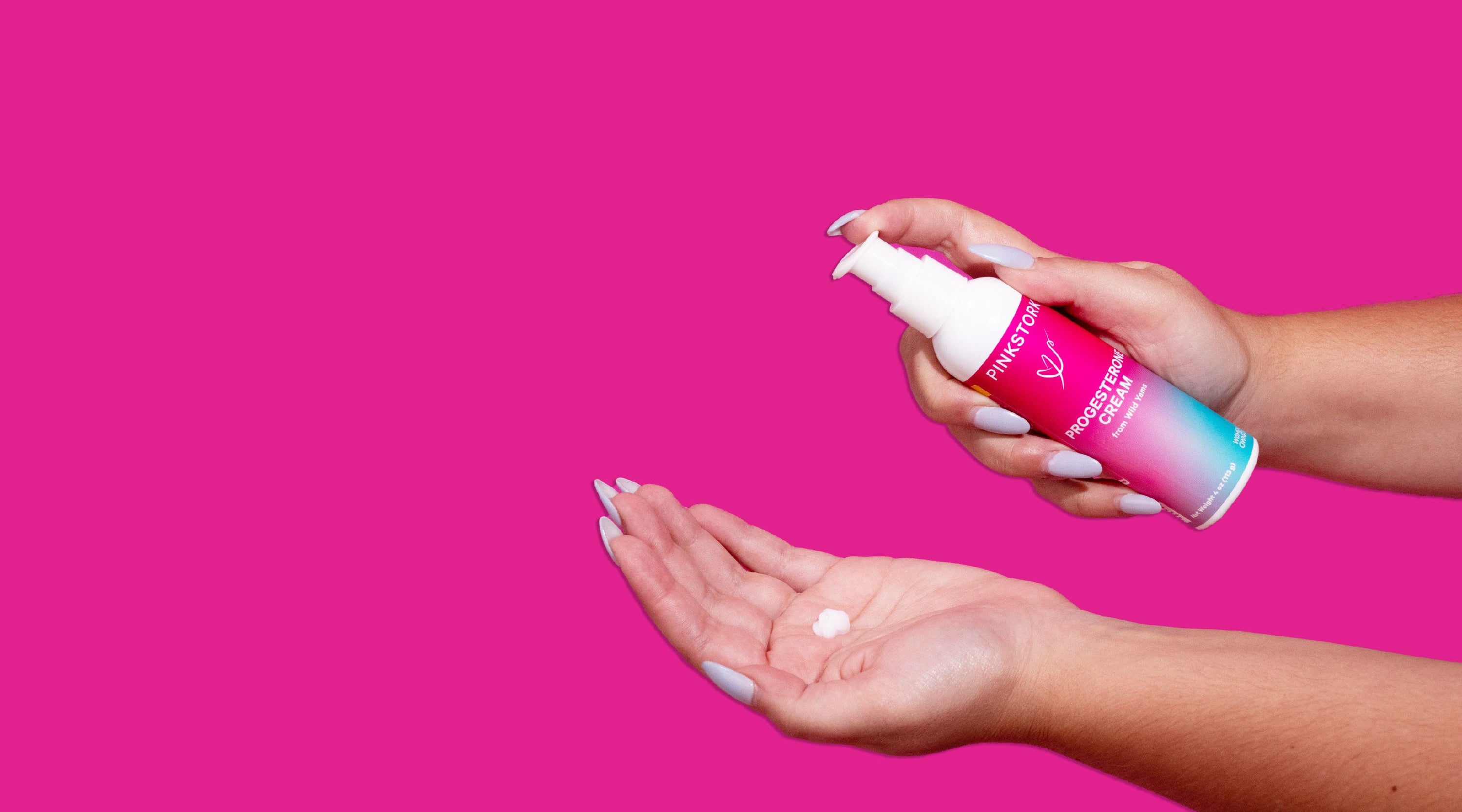 Hands applying Pink Stork postpartum recovery cream from pump bottle against bright pink background.