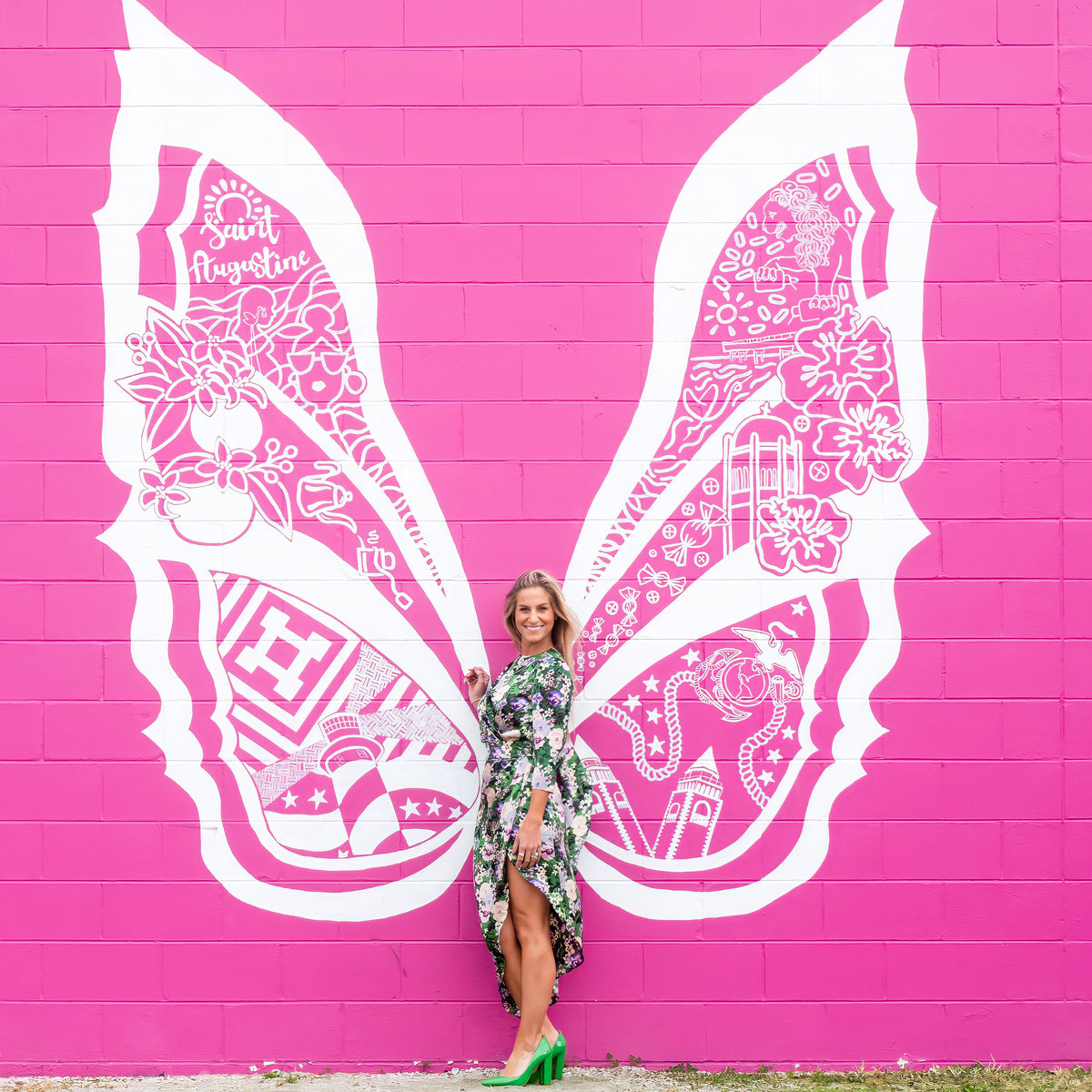 Woman standing next to a large white butterfly mural on a pink wall