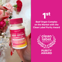 Hand holding a bottle of Pink Stork Beef Organ Complex with flowers in the background and Clean Label Project purity award text.
