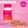 Pink Stork DHA sitting on two thin prisms with DHA gel capsules surrounding the bottom of the bottle. Clinically studied Omega 3s. From sustainably sourced fish.