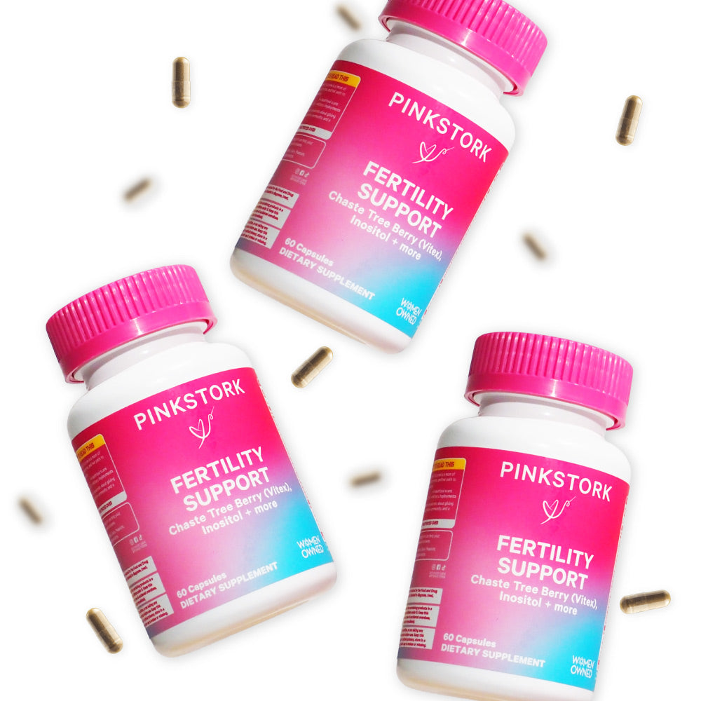 Three bottles of Pink Stork Fertility Support floating with supplement capsules floating around them.