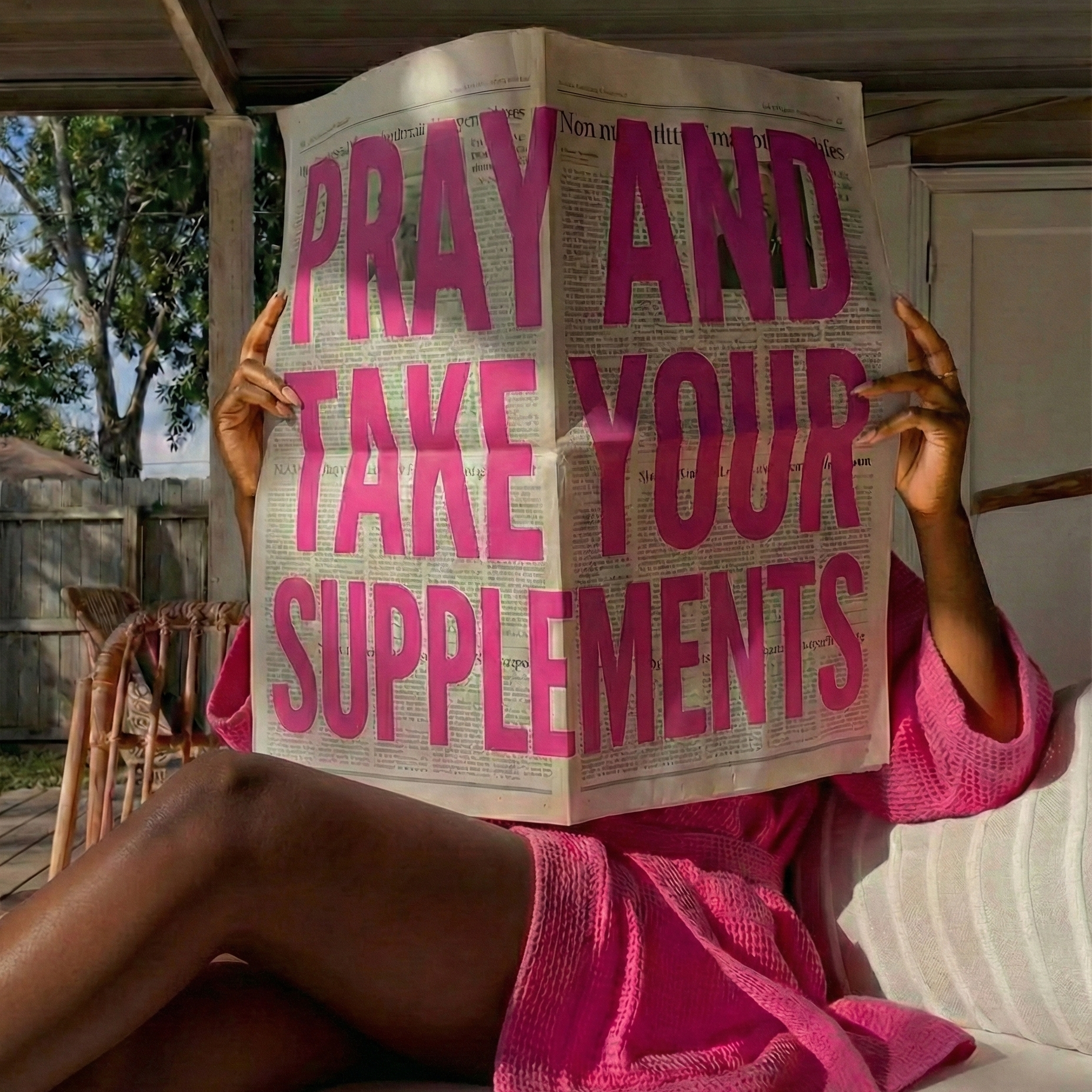 Person holding a newspaper with 'Pray and take your supplements' printed on it, sitting outdoors.