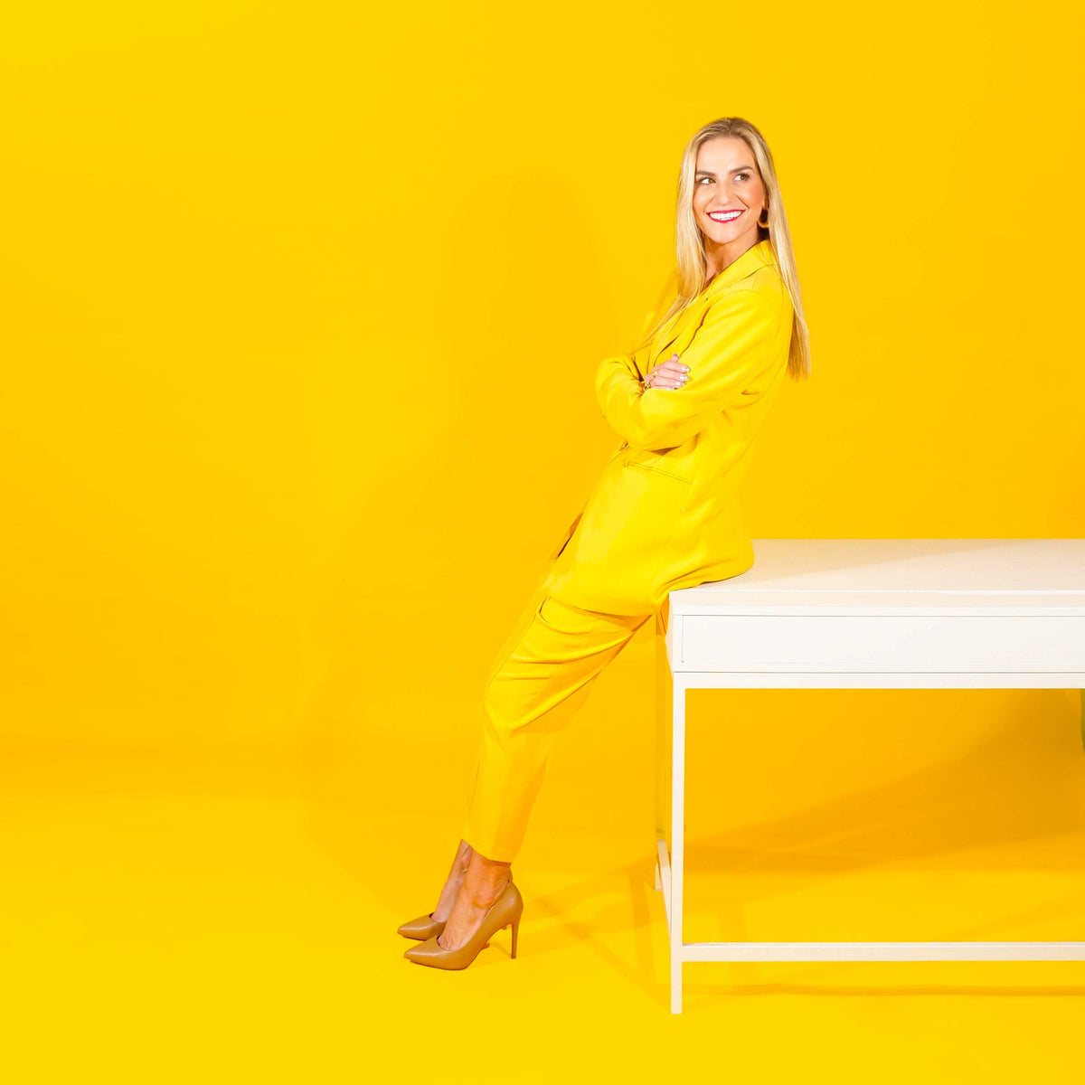 Woman in a yellow outfit sitting on a white bench against a yellow background