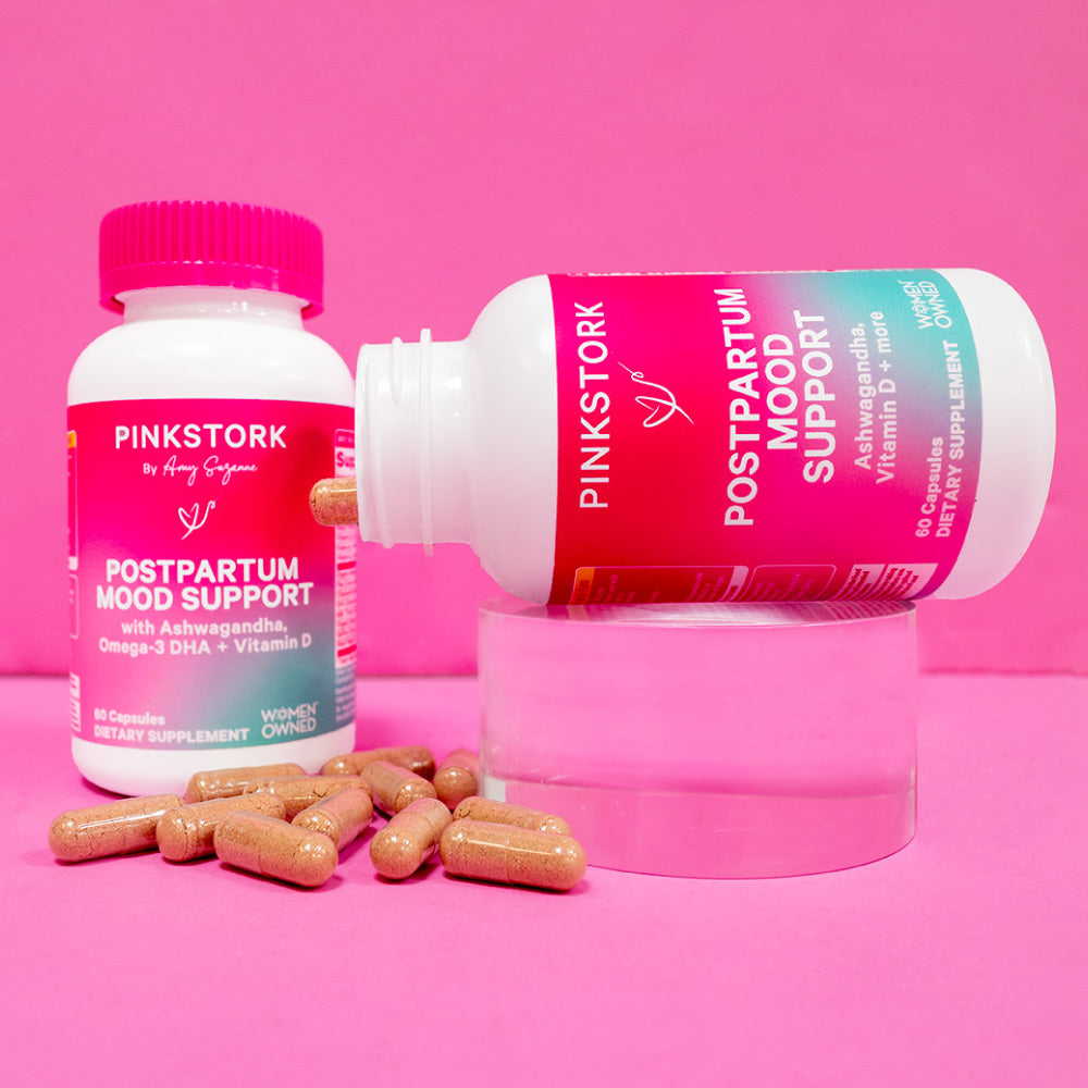 Two bottles of Pink Stork Postpartum Mood Support. One is laying on its side with capsules spilling out of it.