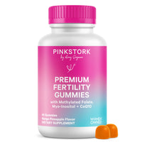 A white bottle of Pinkstork Premium Fertility Gummies with a bright pink cap and a pink-to-blue gradient label, shown on a white background with two orange gummies in front.