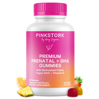 A white bottle of PINKSTORK Premium Prenatal + DHA Gummies with a bright pink cap and a pink-to-orange gradient label. The bottle is centered on a white background with fruit illustrations (pineapple, orange, strawberry, gummy candies) at the bottom.
